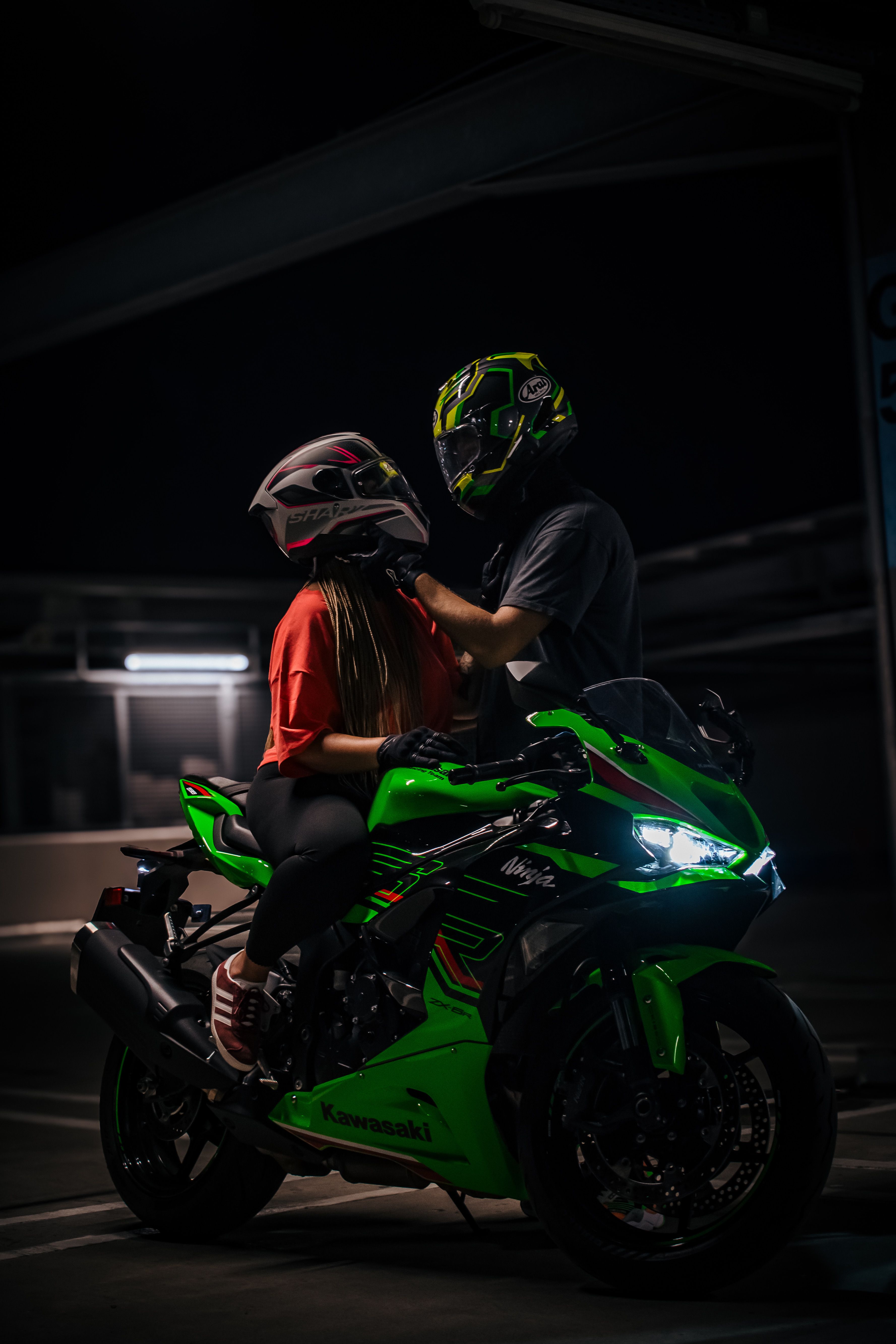 Two people on a green motorcycle preparing to ride at night.