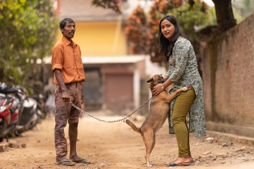 A man and woman outdoors bonding with a pet dog on a sunny urban street.