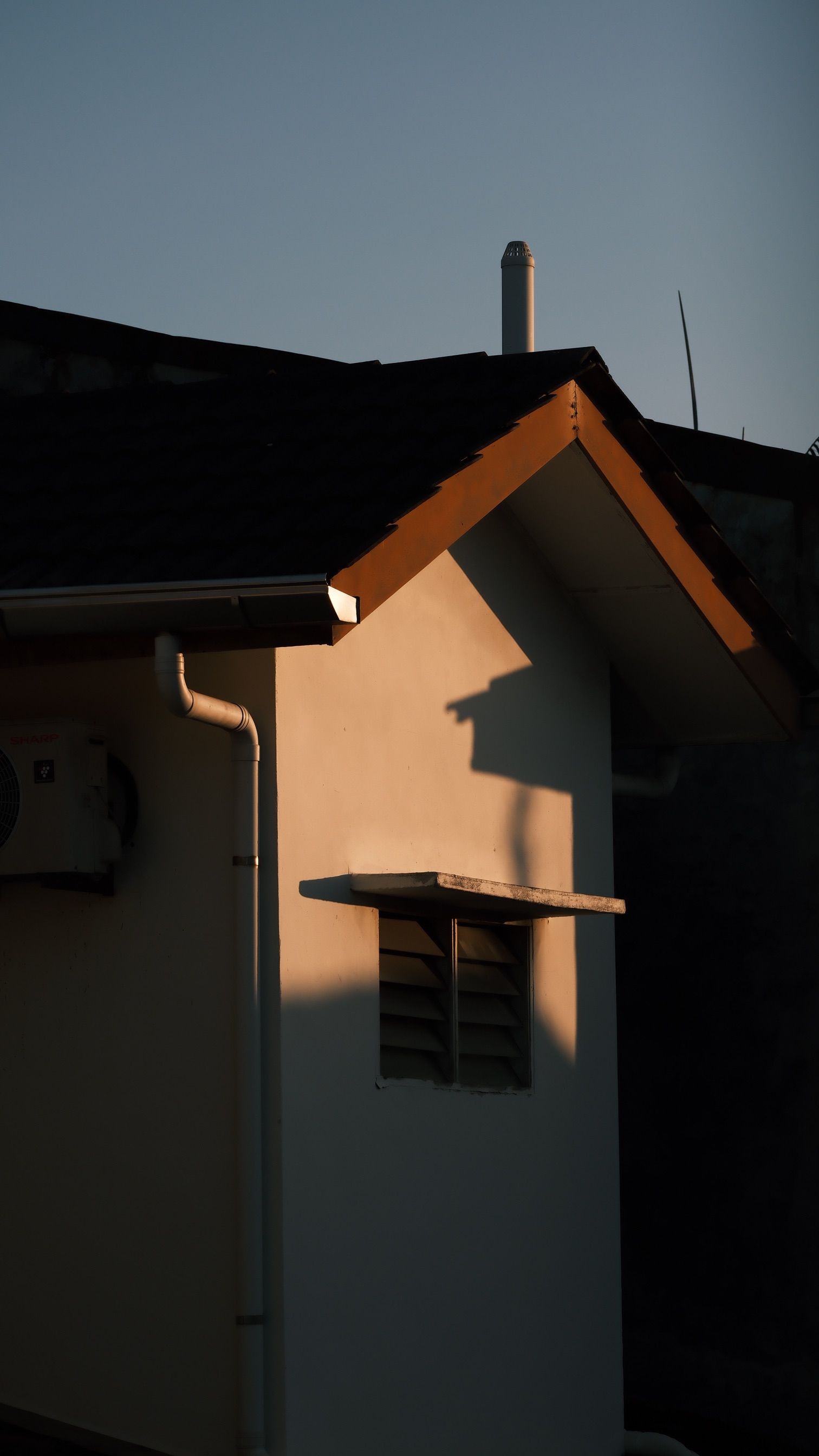 Warm sunlight casts shadows on a modern house facade during sunset.