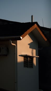 Warm sunlight casts shadows on a modern house facade during sunset.