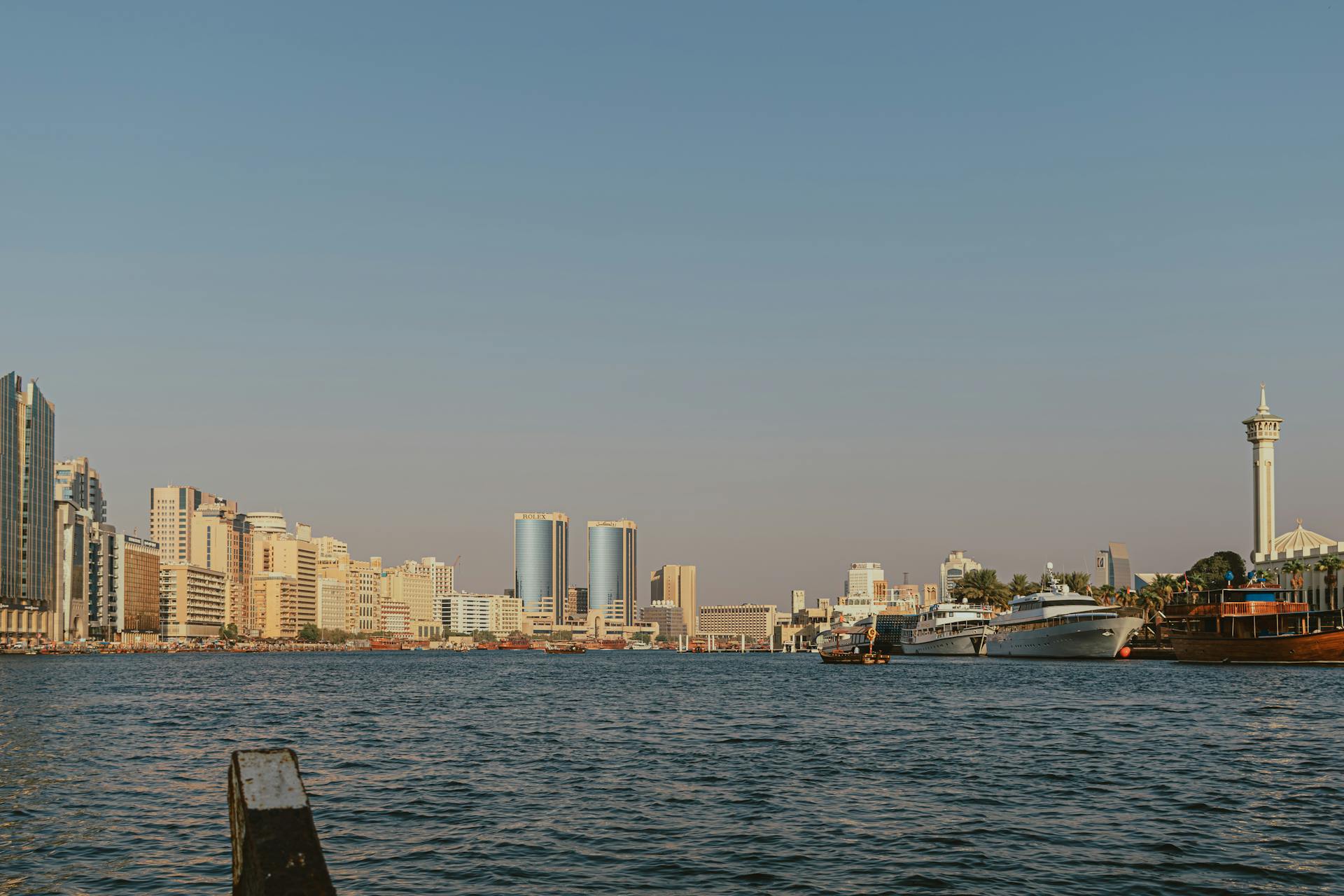 A stunning view of Dubai's skyline at sunset, featuring boats on Dubai Creek and iconic city architecture.