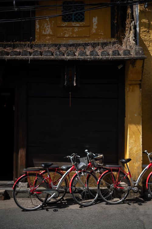 Free Three red bicycles against a yellow ancient wall in the vibrant streets of Hội An, Vietnam. Stock Photo
