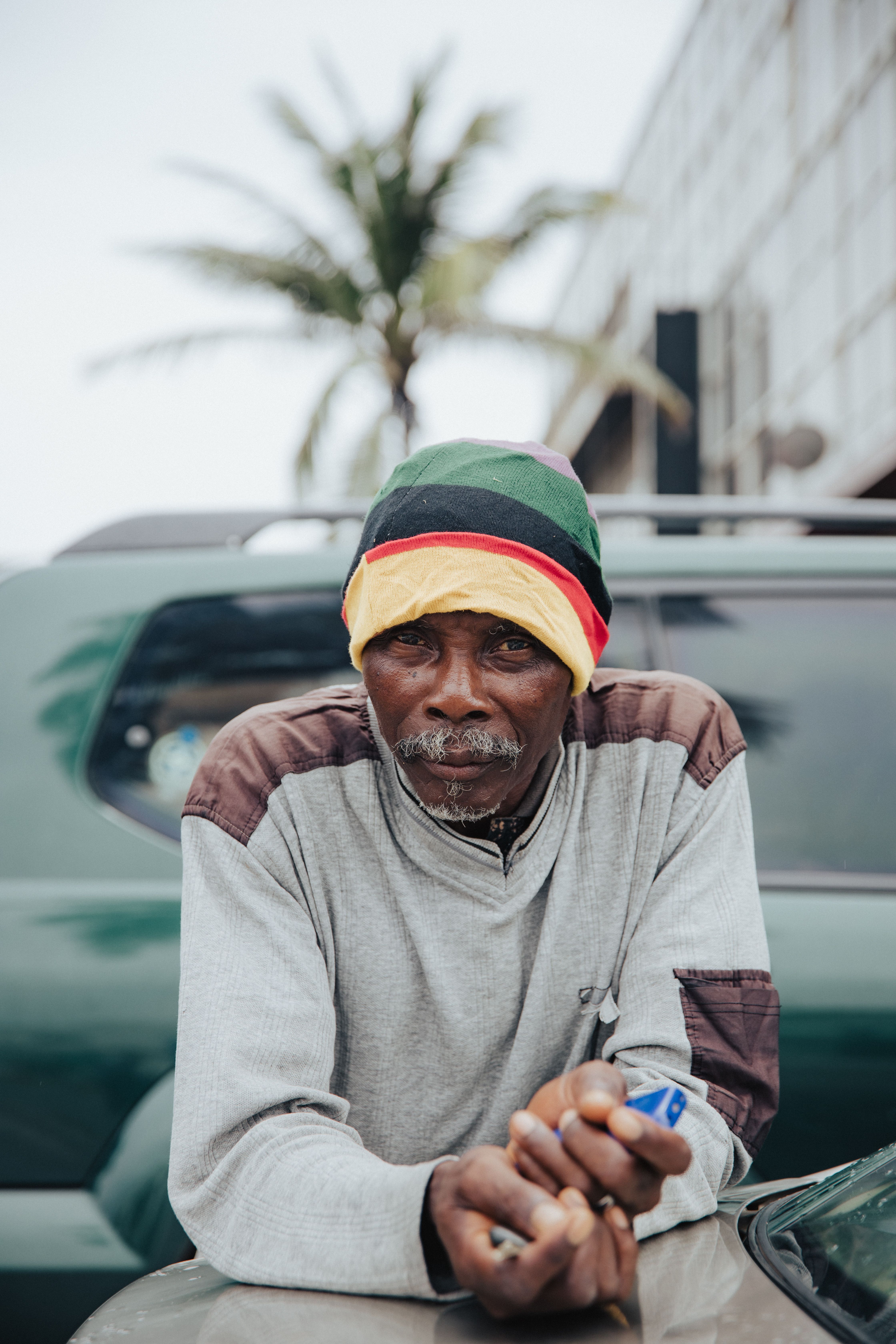 A man with a colorful hat sitting in front of a car · Free Stock Photo