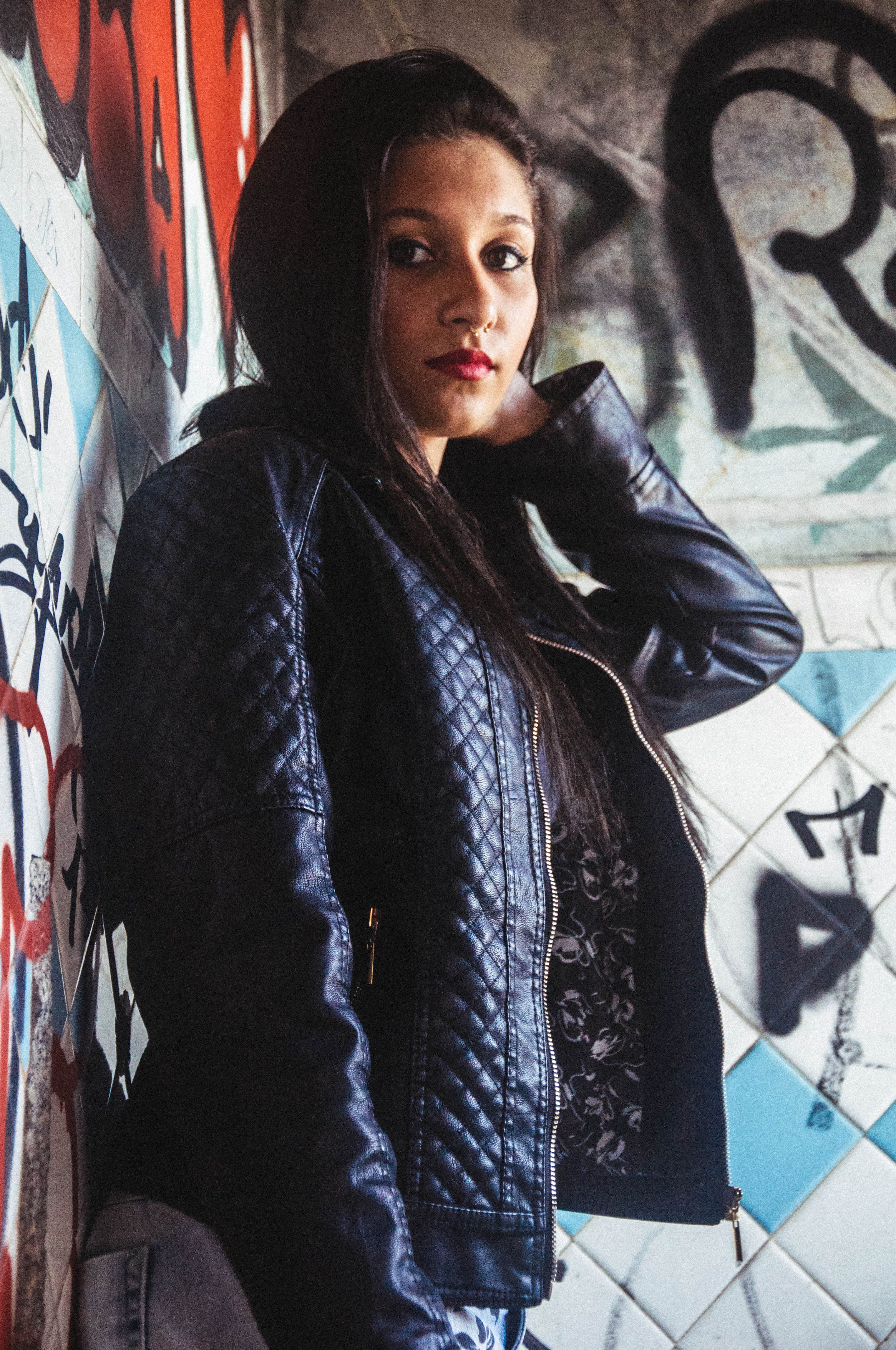 A woman in a leather jacket leaning against a wall · Free Stock Photo