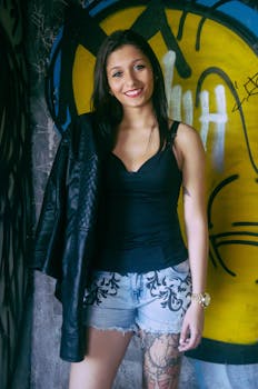 Confident woman in fashionable attire poses against vibrant graffiti wall, expressing individuality.