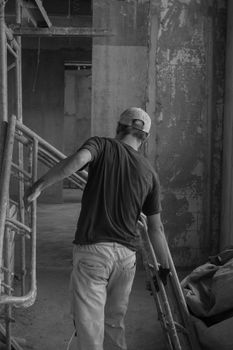 Worker adjusting scaffolding in an industrial indoor setting captured in monochrome.