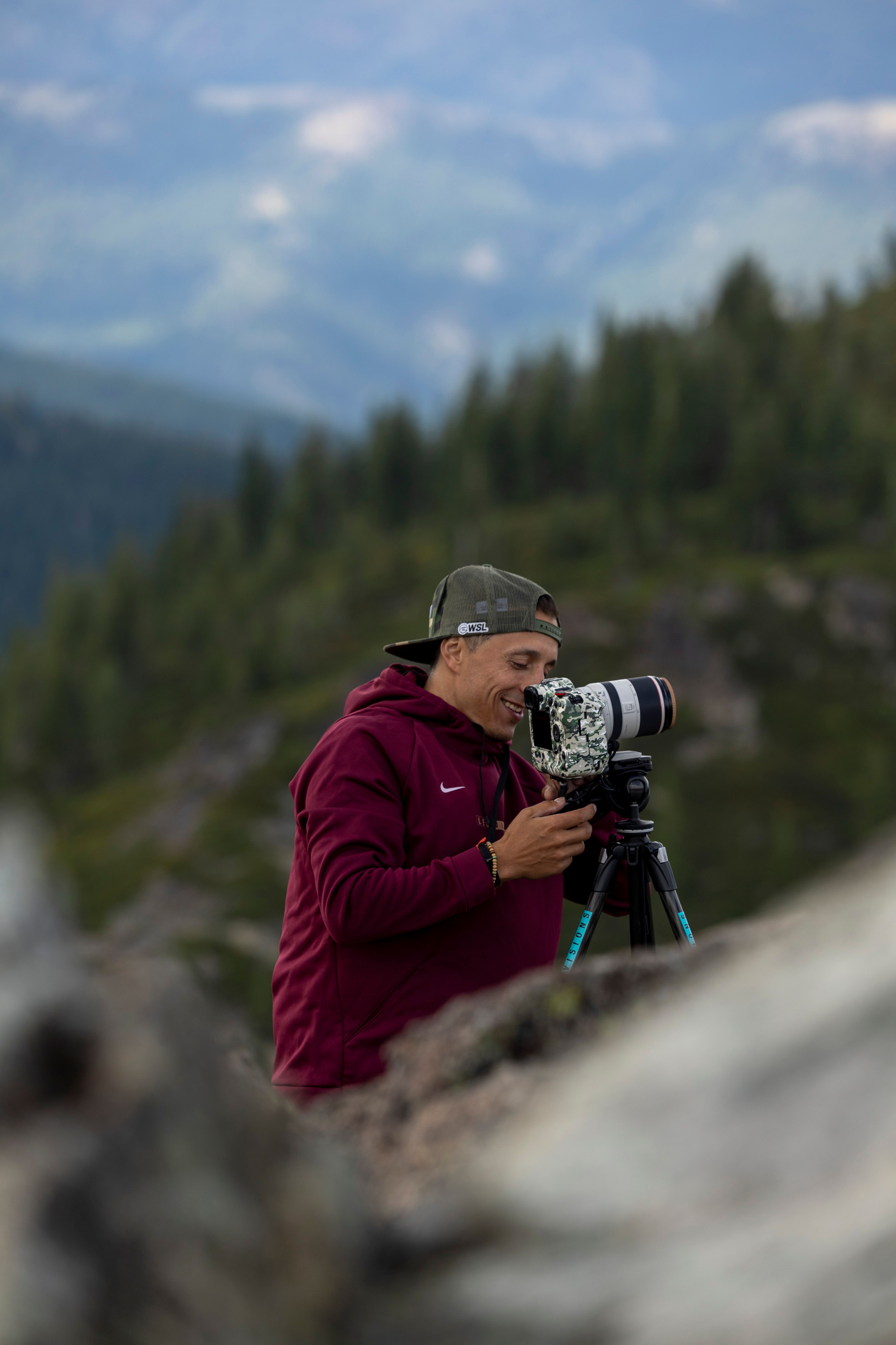 Photographer using DSLR on tripod in scenic winter mountain setting for a nature shot.