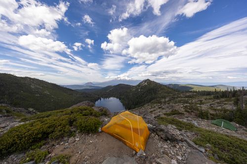 Free A vibrant tent overlooking a serene lake and majestic mountains under a clear sky, perfect for adventure seekers. Stock Photo