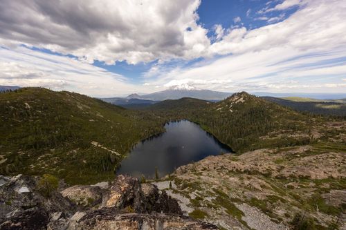 Free Stunning view of a mountain lake surrounded by lush hills and distant peaks under a dramatic sky. Stock Photo