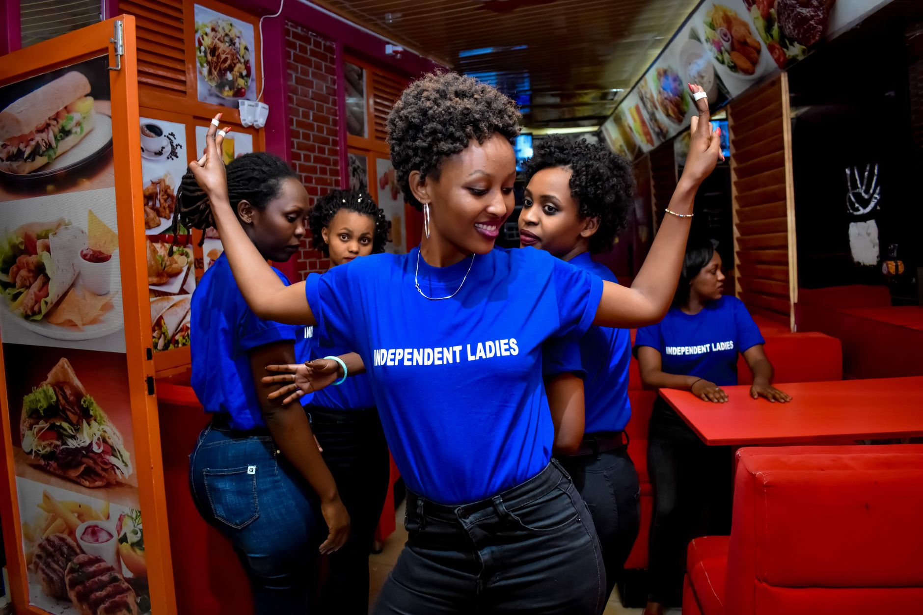A group of stylish women in matching 'Independent Ladies' shirts gathering indoors with vibrant decor.