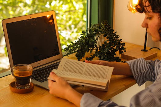 Warm indoor setting with a laptop, coffee, and book creating a cozy workspace.