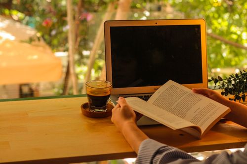 Free Person enjoying a book and coffee outdoors with a laptop, perfect for relaxation. Stock Photo
