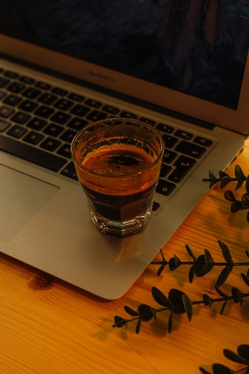 Free Shot of espresso resting on a laptop next to green leaves, creating a cozy workspace vibe. Stock Photo