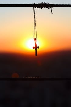 十字吊坠悬挂在充满活力的日落天空中，捕捉到一个宁静而灵性的时刻
