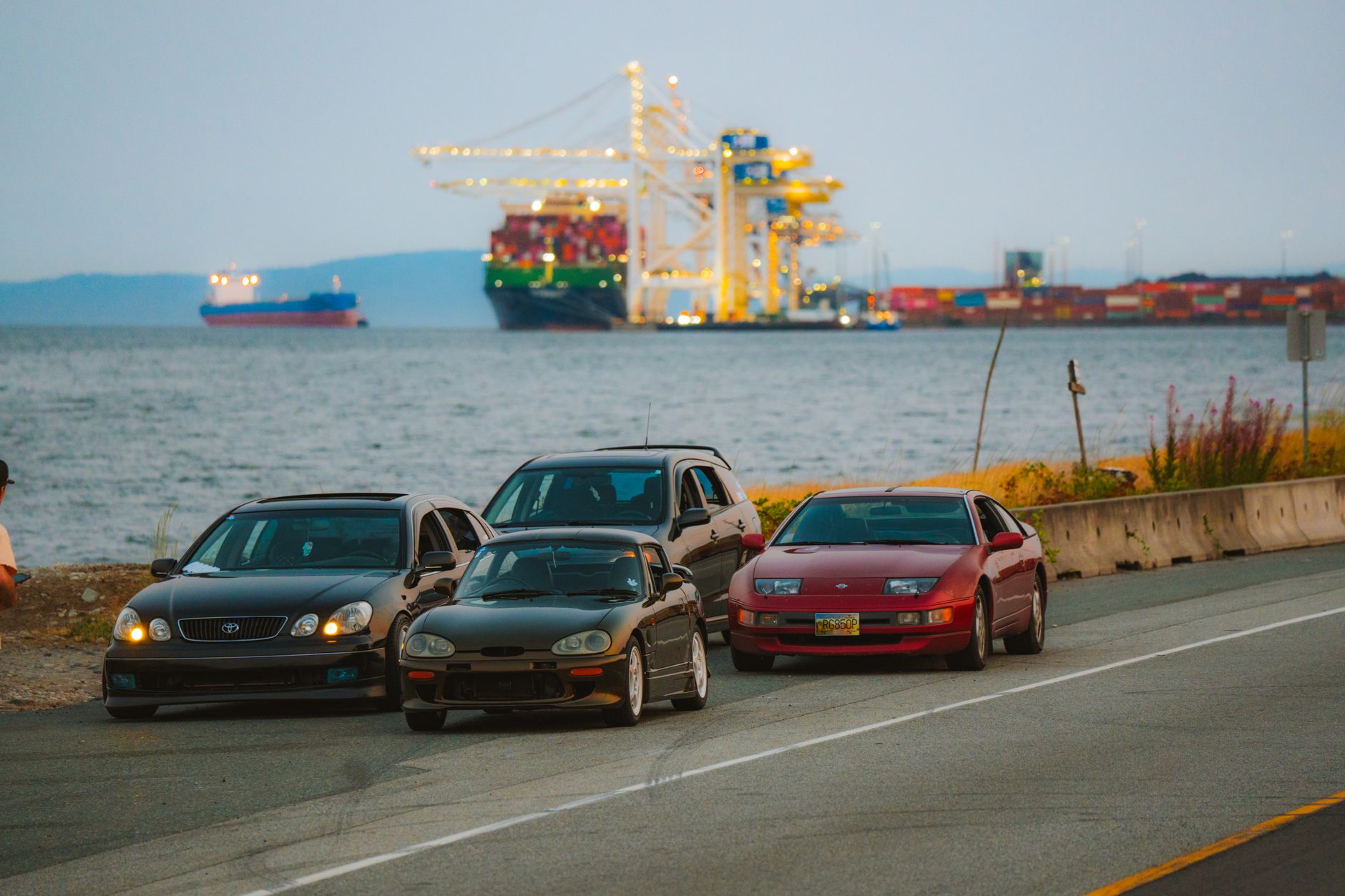 2025년 자동차 관세 인상 논의, 현대차 주가에 미치는 경제적 영향 심층 분석 3 Three parked cars by the seashore with cargo ships and cranes at a harbor nearby, during the day.