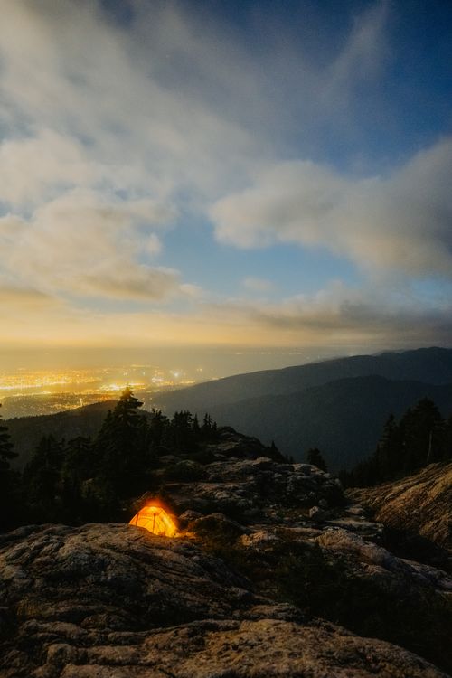 Free Enjoy breathtaking views from a mountain campsite overlooking a glowing cityscape at twilight. Stock Photo