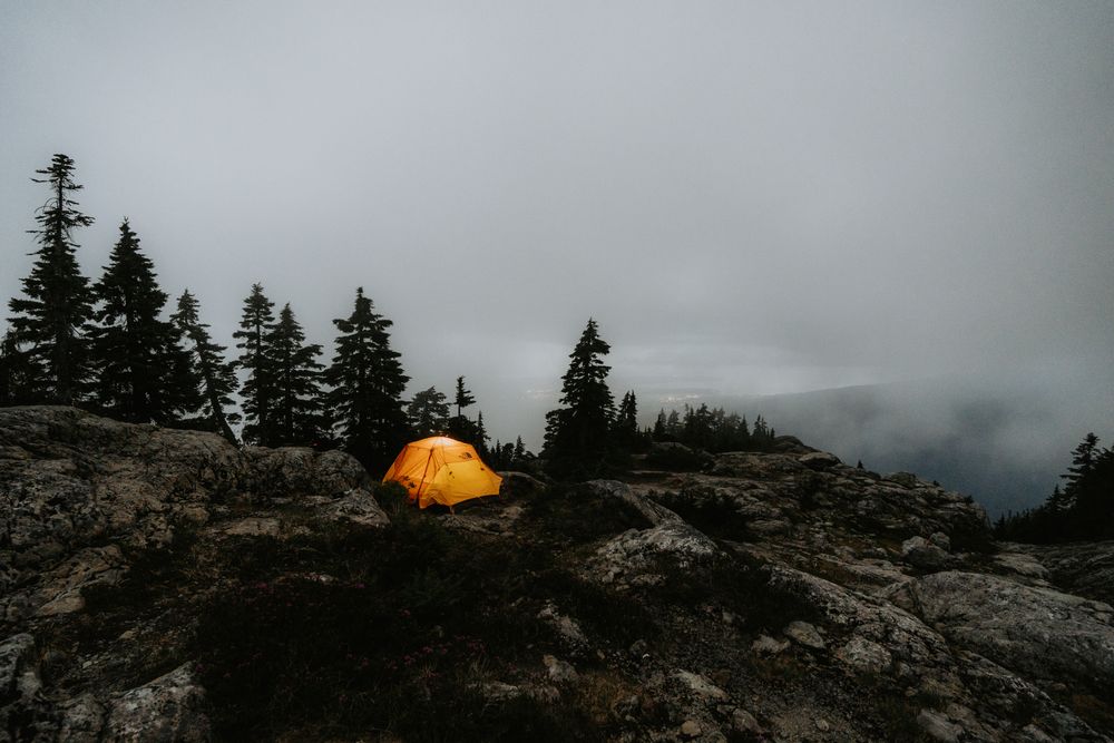 A single tent glowing at dawn on a fog covered ridge