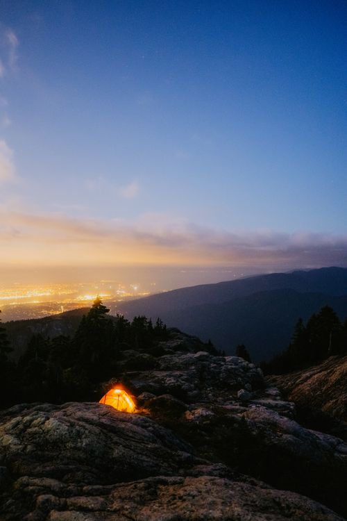Free A mesmerizing view of a tent on a mountain with city lights at twilight. Perfect for adventure and travel themes. Stock Photo