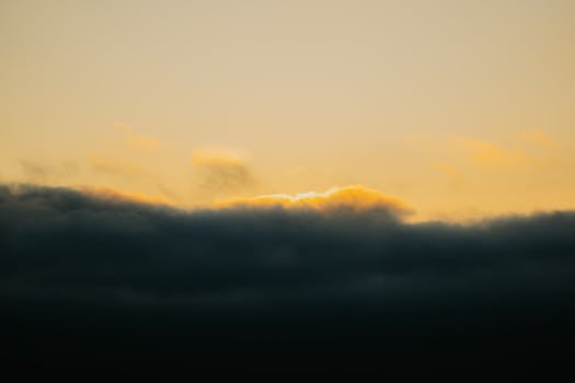 A serene sunset with dramatic clouds and warm hues over a silhouetted landscape.