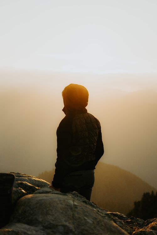 Free A solitary figure silhouetted against a stunning mountain sunset, capturing a moment of reflection and serenity. Stock Photo