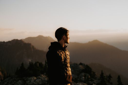 A man overlooks misty mountains at sunset, embracing adventure.