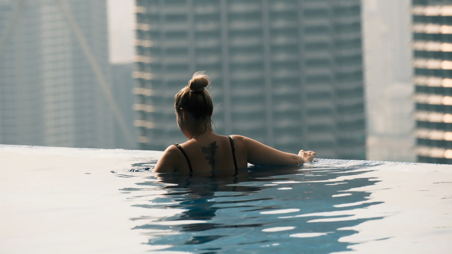 A woman enjoys a peaceful swim in a rooftop infinity pool overlooking a cityscape.