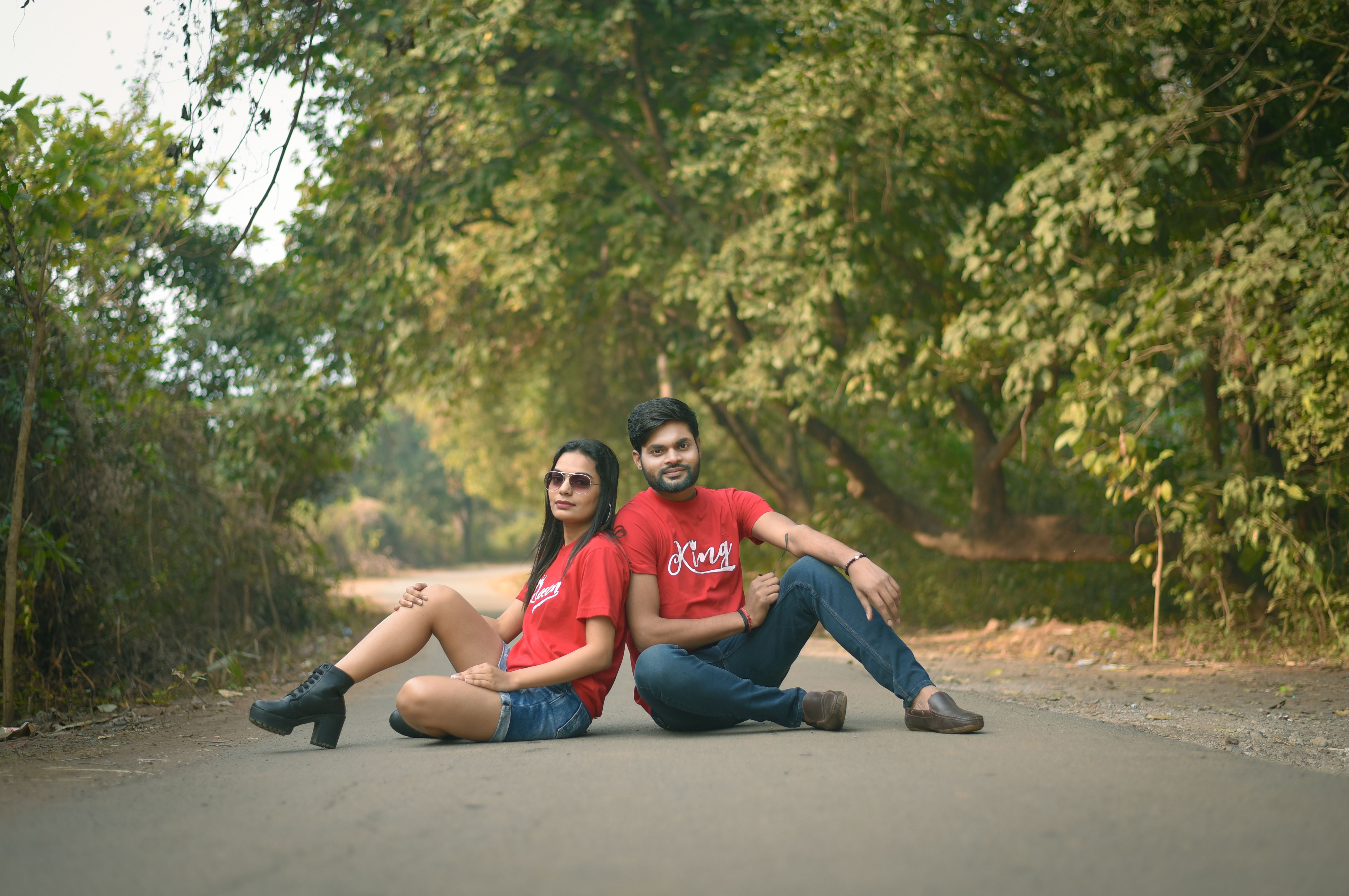 A couple in matching red shirts sits on a road in a lush green park, enjoying a moment of relaxation.