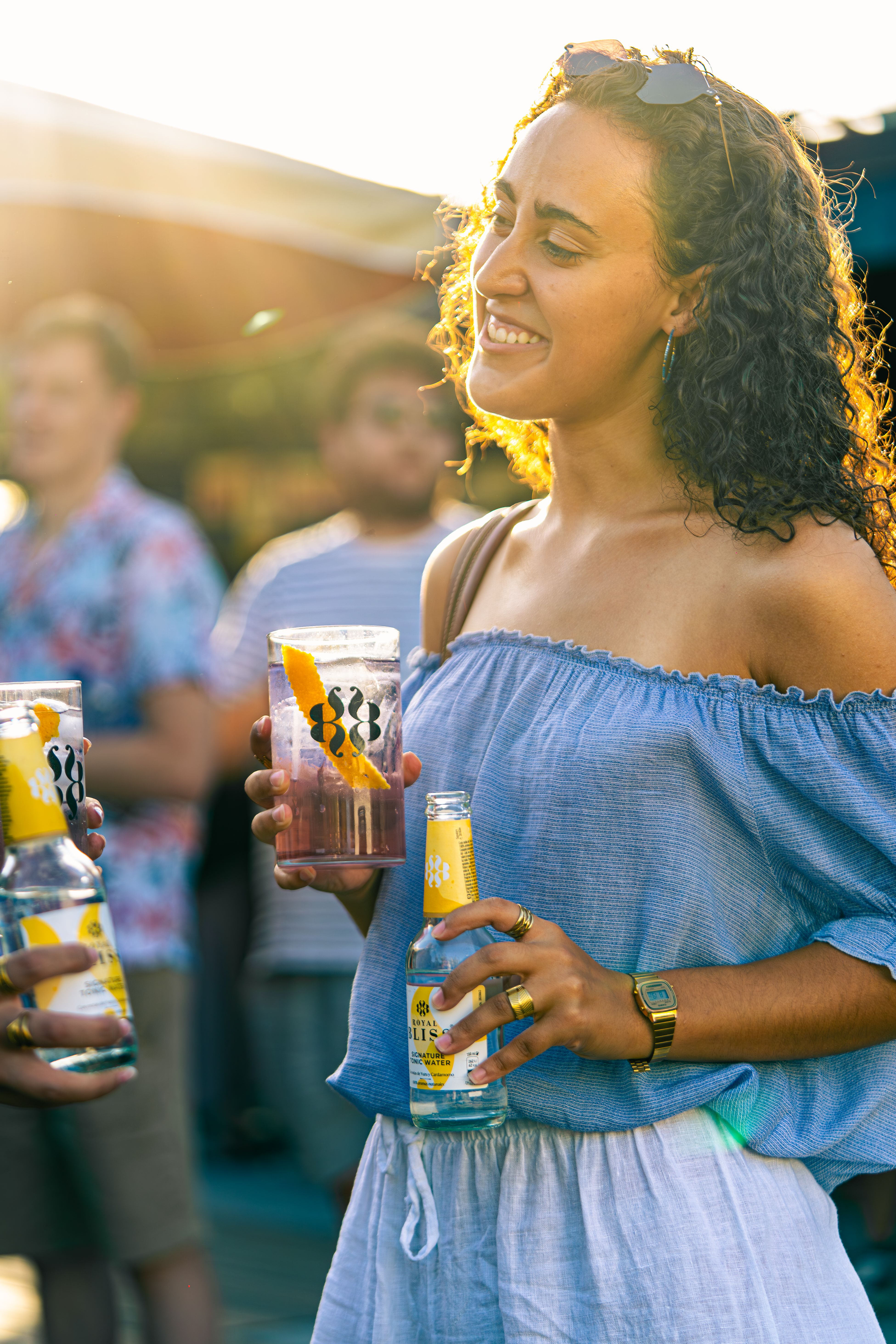 Smiling woman holding drinks at a lively outdoor summer party.