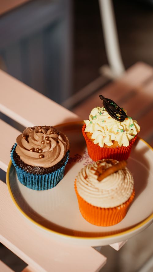 Free A plate of three colorful cupcakes with chocolate and cream toppings, perfect for sweets lovers. Stock Photo