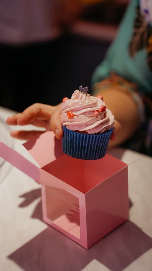 Free Close-up of a hand placing a pink frosted cupcake into a pink gift box. Stock Photo