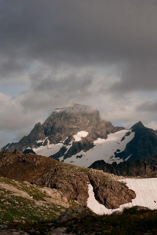Free Majestic mountains with snow patches under moody clouds create a dramatic scene. Stock Photo