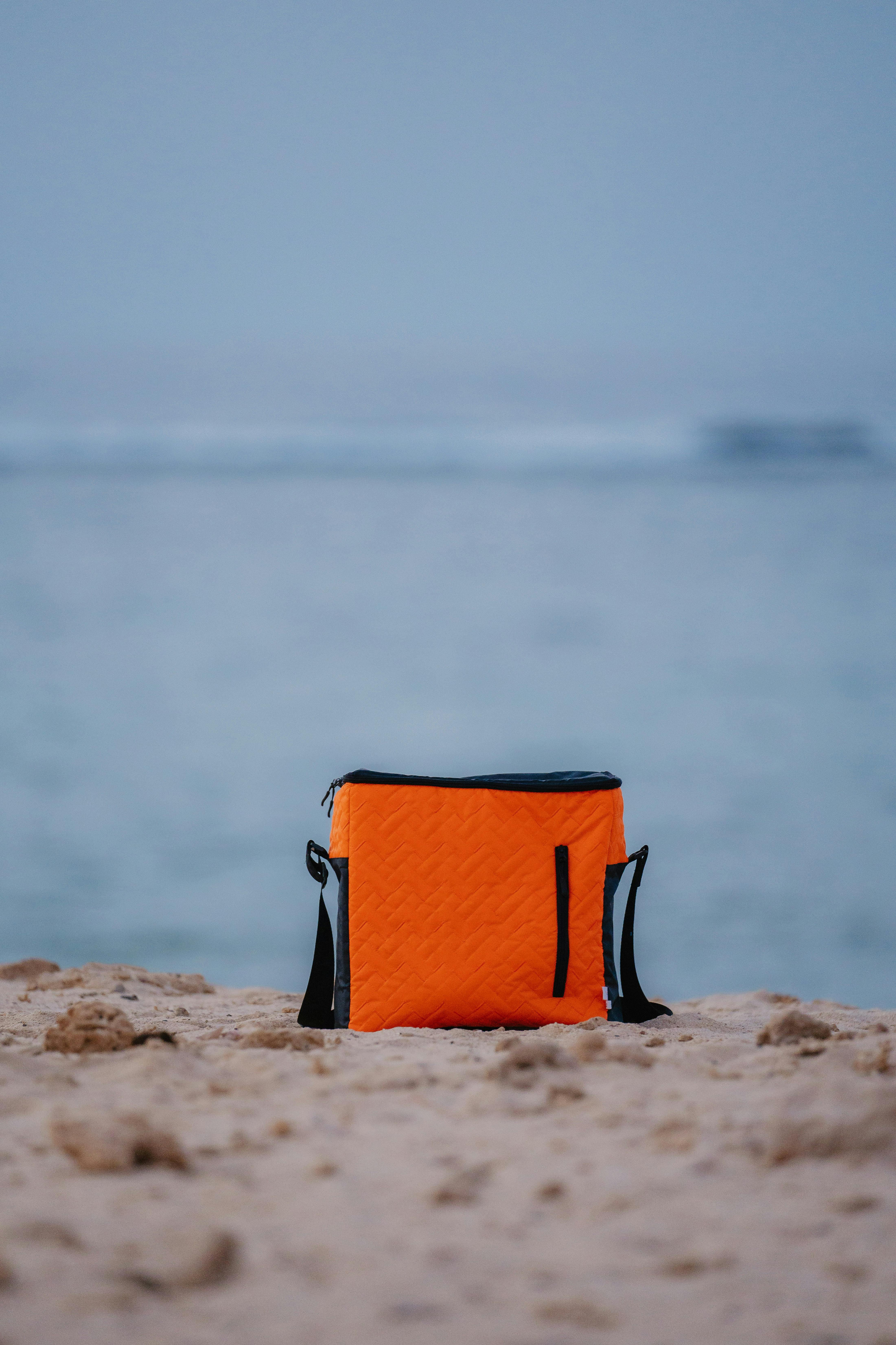 Bright orange cooler bag resting on a sandy beach in Marsa Alam, Egypt, by the Red Sea shore.