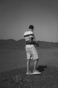 A man with a camera stands on a rocky hill in Marsa Alam, Egypt, capturing the vast desert landscape.