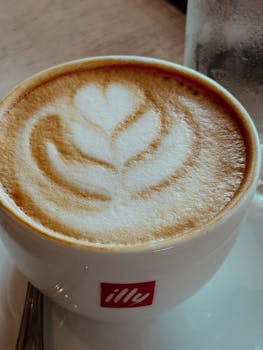 A warm cappuccino with intricate latte art, served in a branded Illy cup.