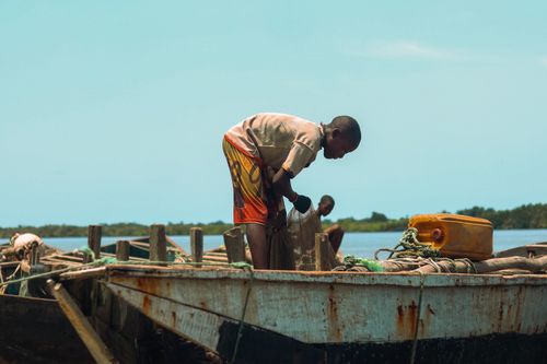 Free A young boy works on a fishing boat by a calm river, preparing for a fishing day. Stock Photo