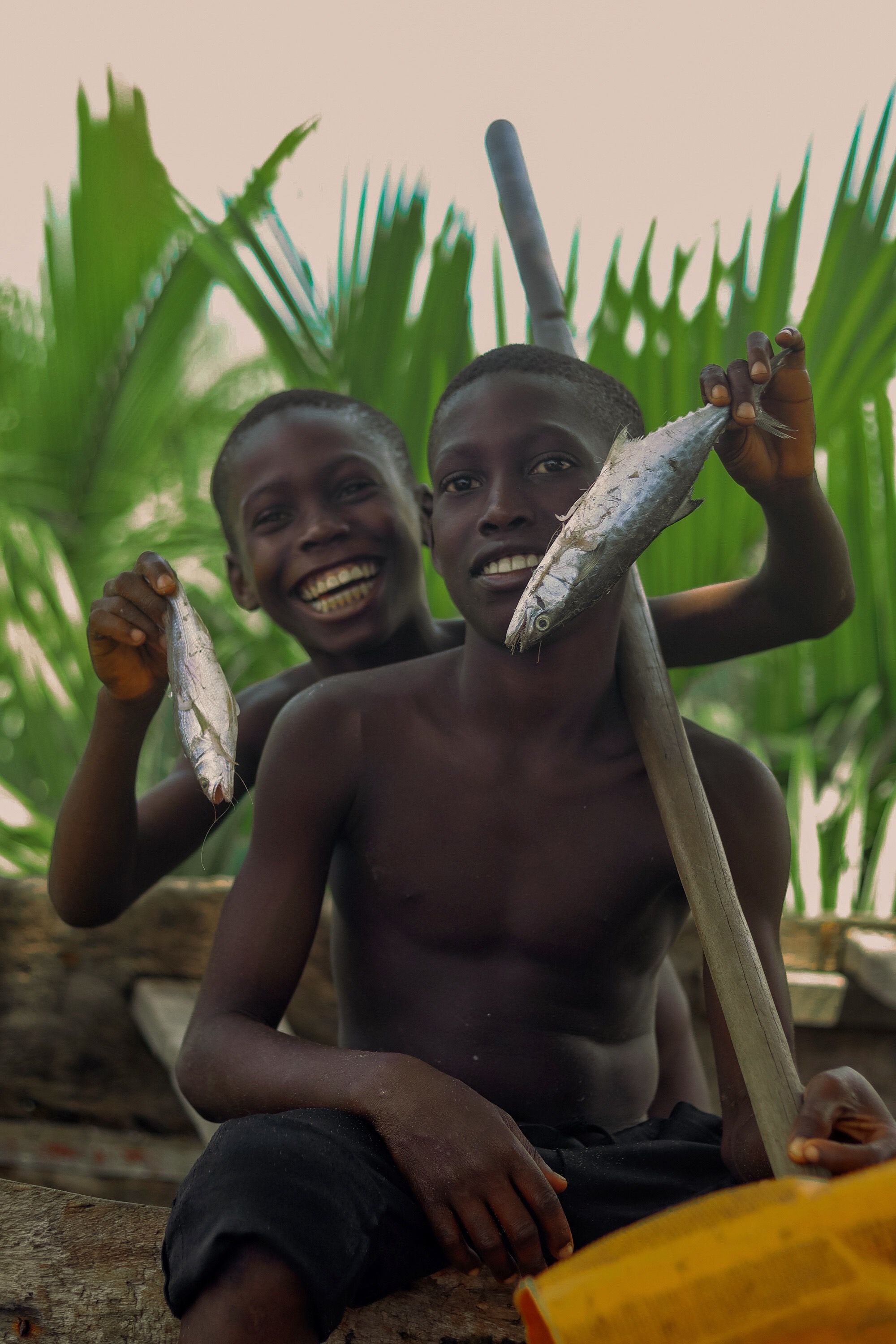 Two boys happily displaying their catch of fish, creating a cheerful outdoor scene full of life.