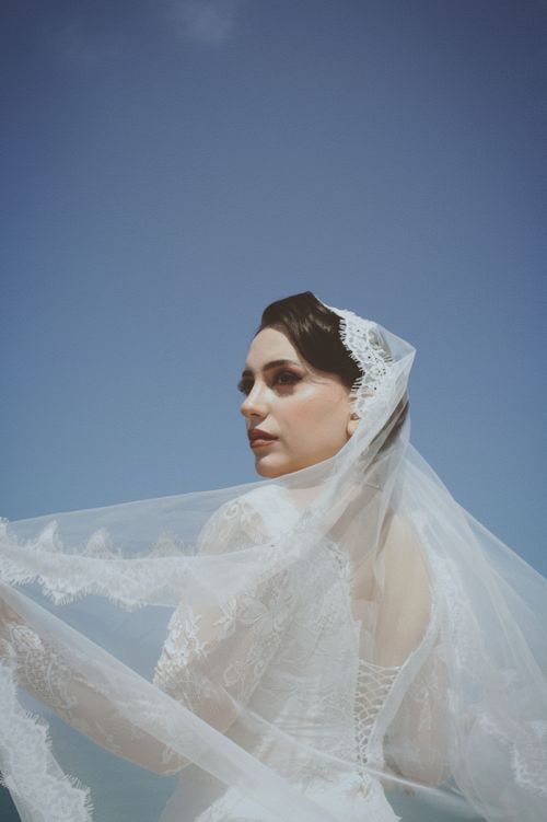 Free Elegant bride in lace veil gazes under clear sky. Perfect for wedding themes. Stock Photo