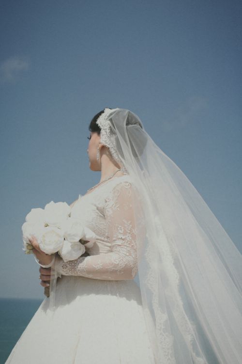 Free Elegant bridal portrait with bouquet and veil by the sea in daylight. Stock Photo