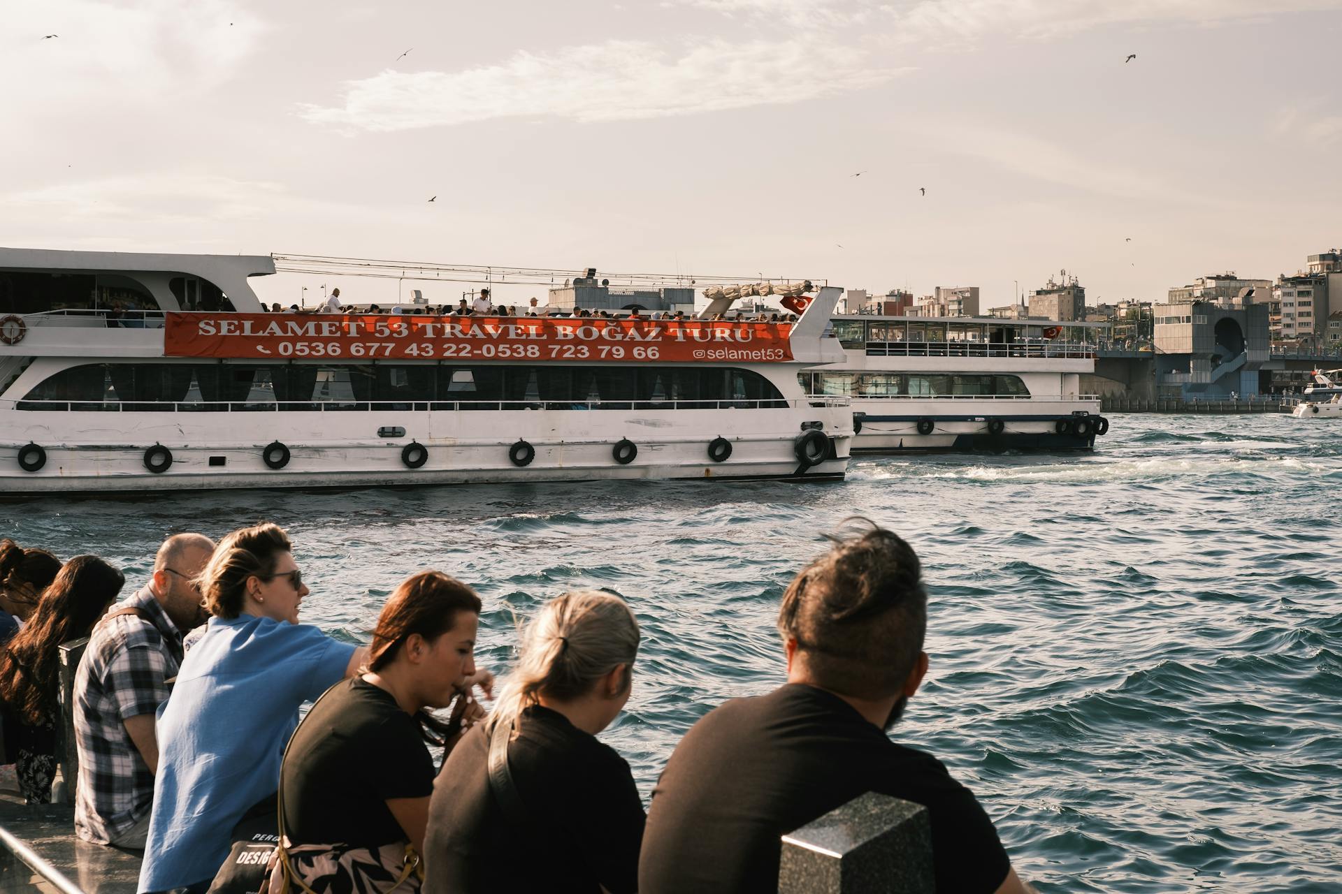 Ferry cruising on Istanbul waters with tourists and cityscape backdrop.