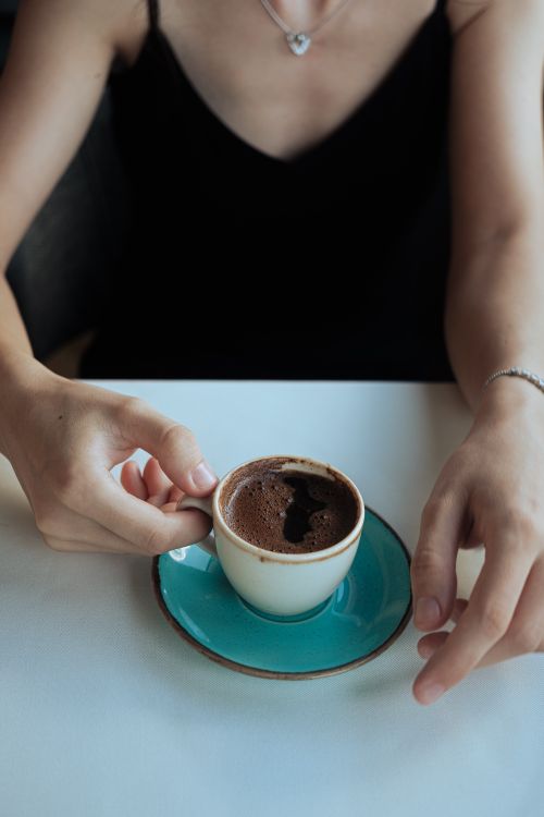 Free A woman enjoys a cup of dark coffee in a turquoise saucer, creating a serene morning moment. Stock Photo