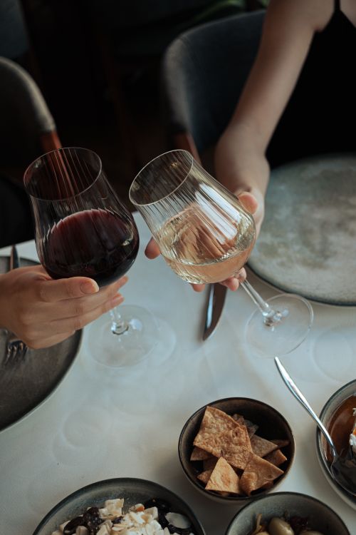 Free Two people toasting with red and white wine glasses over a dinner table. Stock Photo