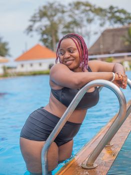 Young woman in swimwear relaxing by the pool on a summer day, smiling joyfully.