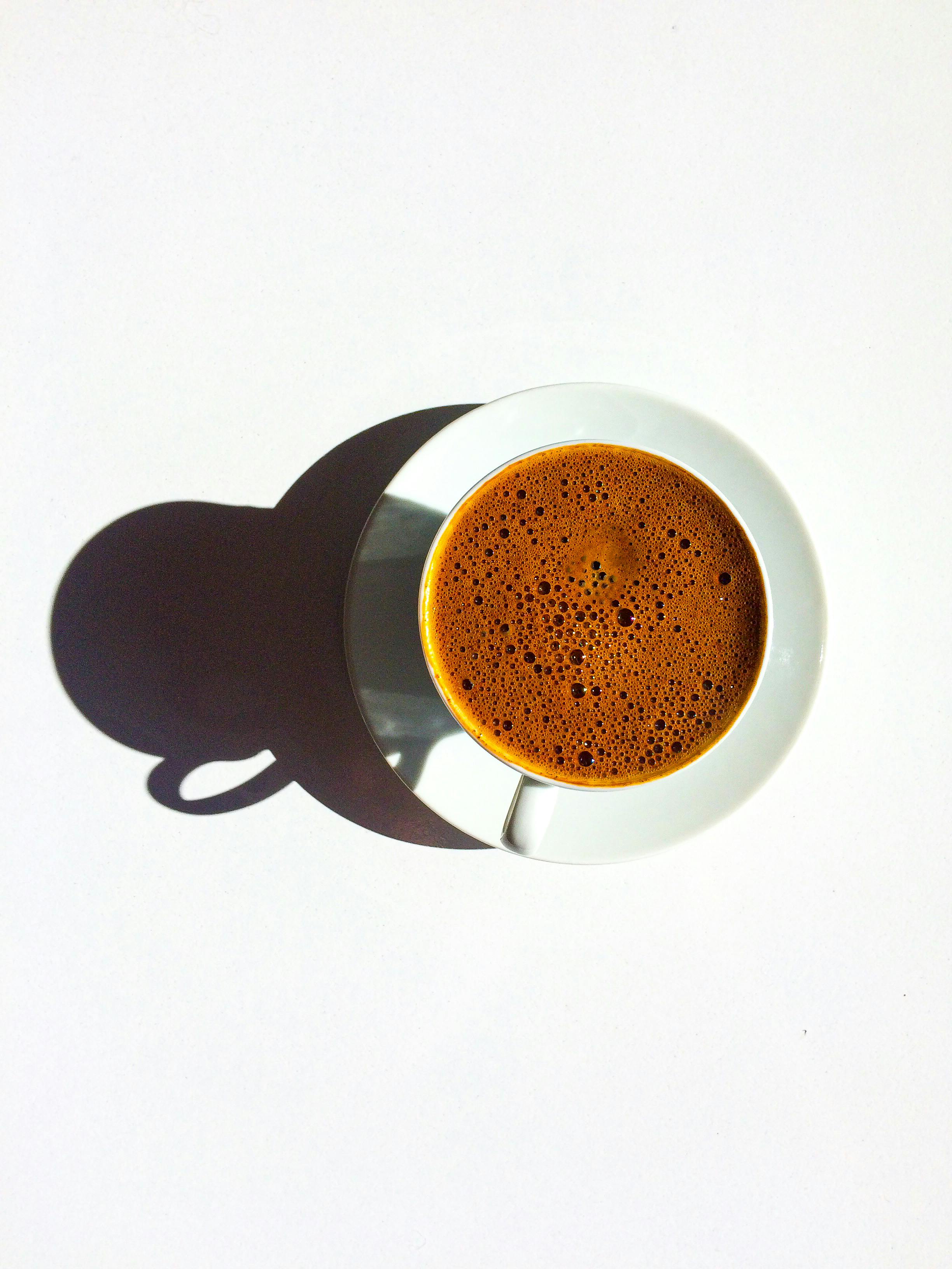 A minimalist top-down view of a coffee cup casting a shadow on a white surface.