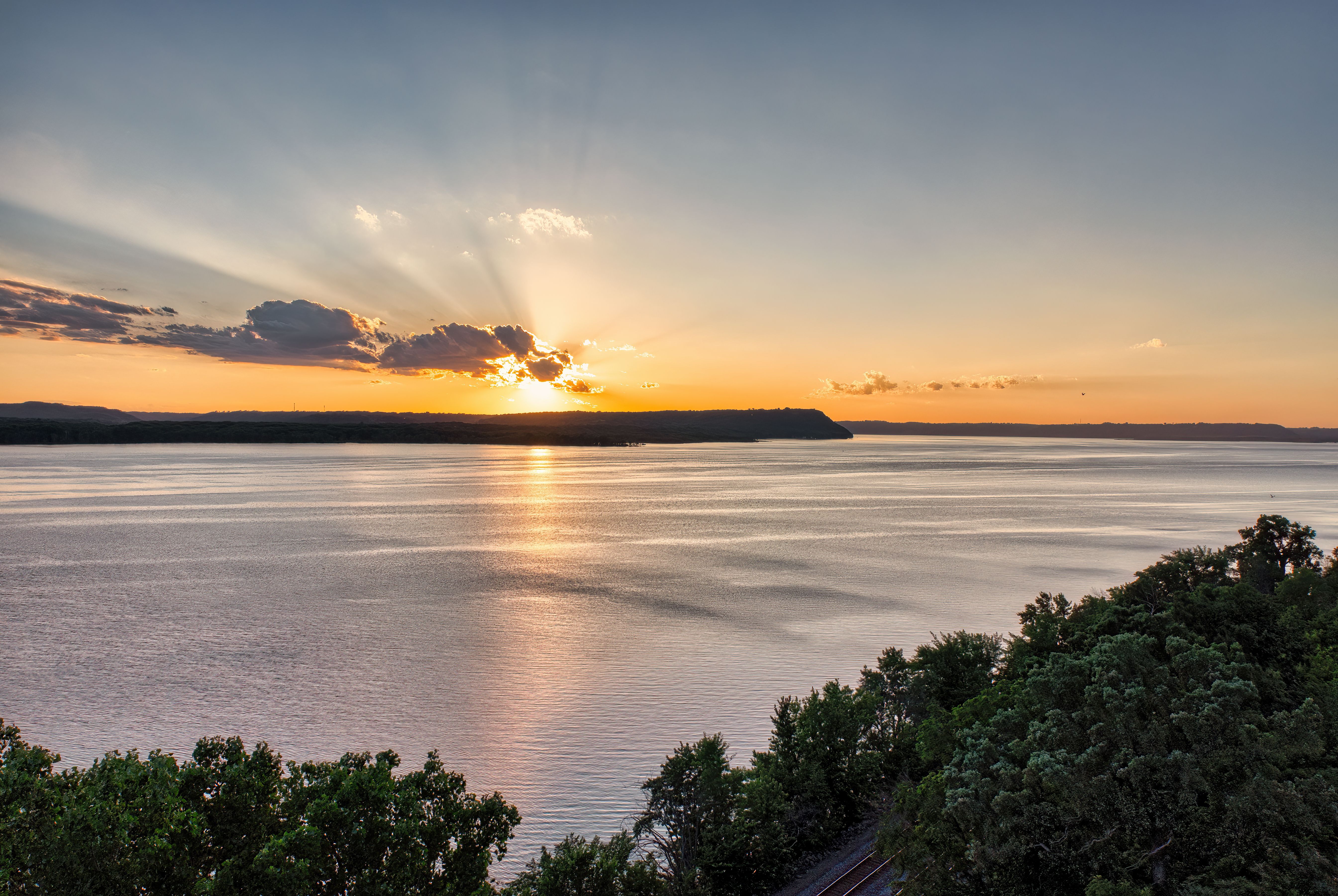 A sunset over a body of water with trees and hills · Free Stock Photo