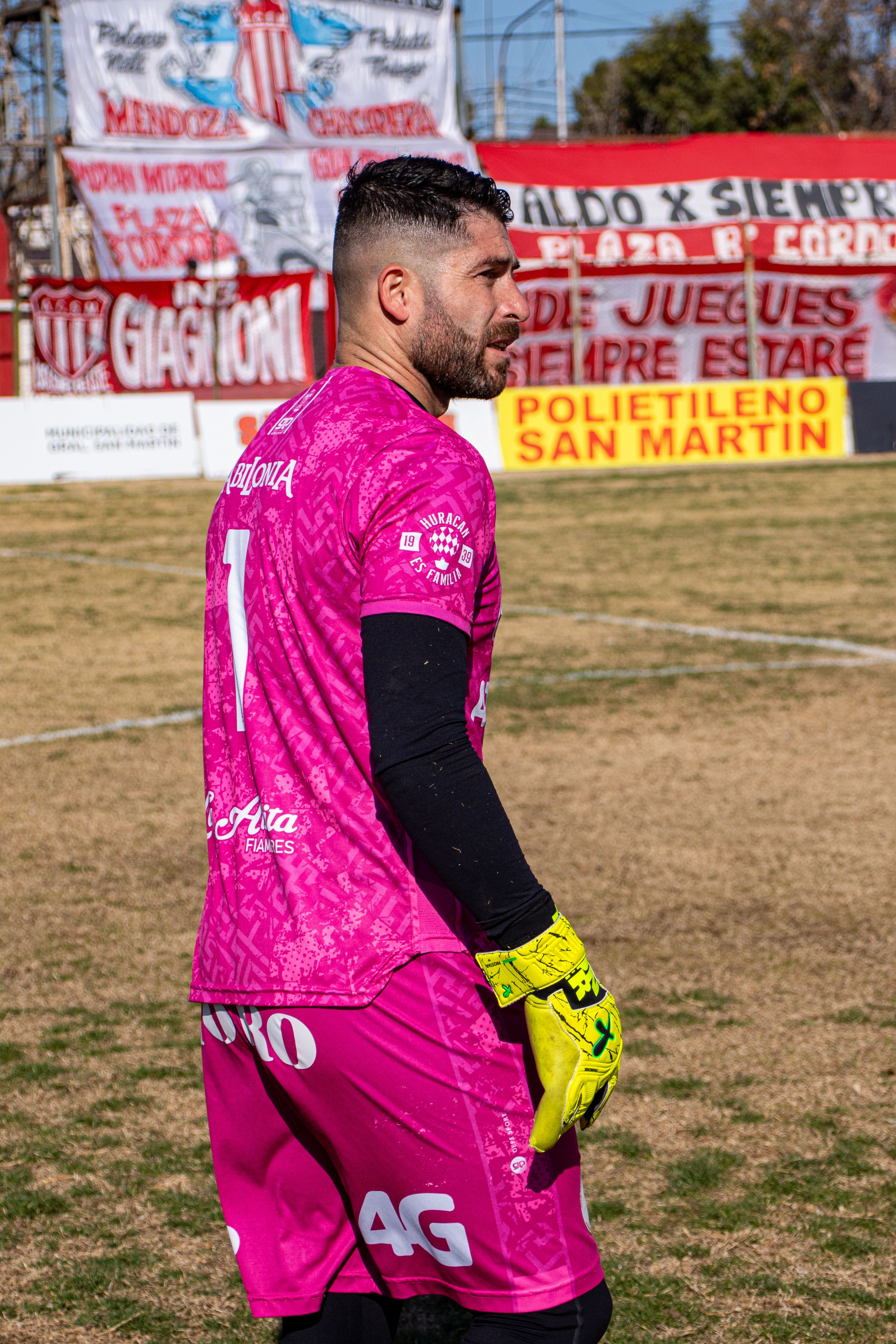 Goalkeeper in pink jersey standing on soccer field with colorful banners.