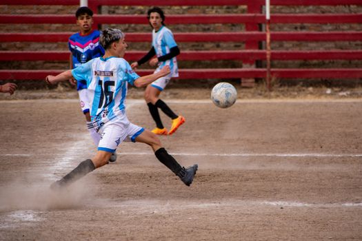 Dynamic moment of teens playing soccer on a dirt field, displaying skill and teamwork.