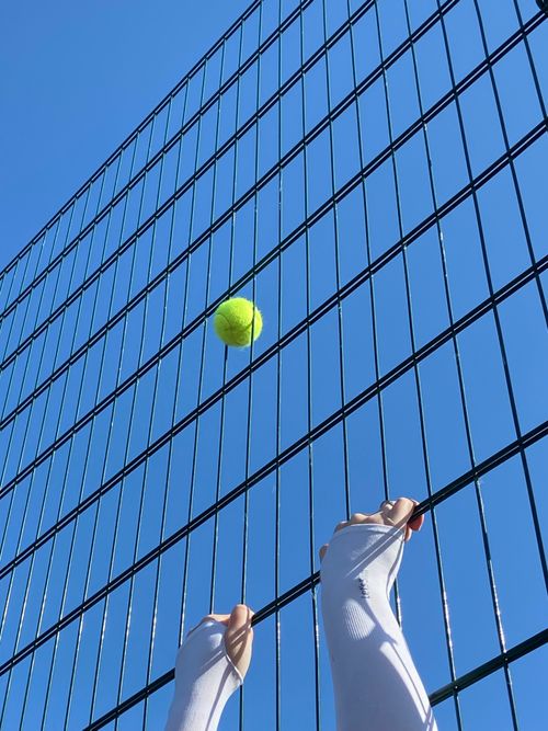 Free Tennis ball in action against a wire fence and blue sky, highlighting motion in sports. Stock Photo