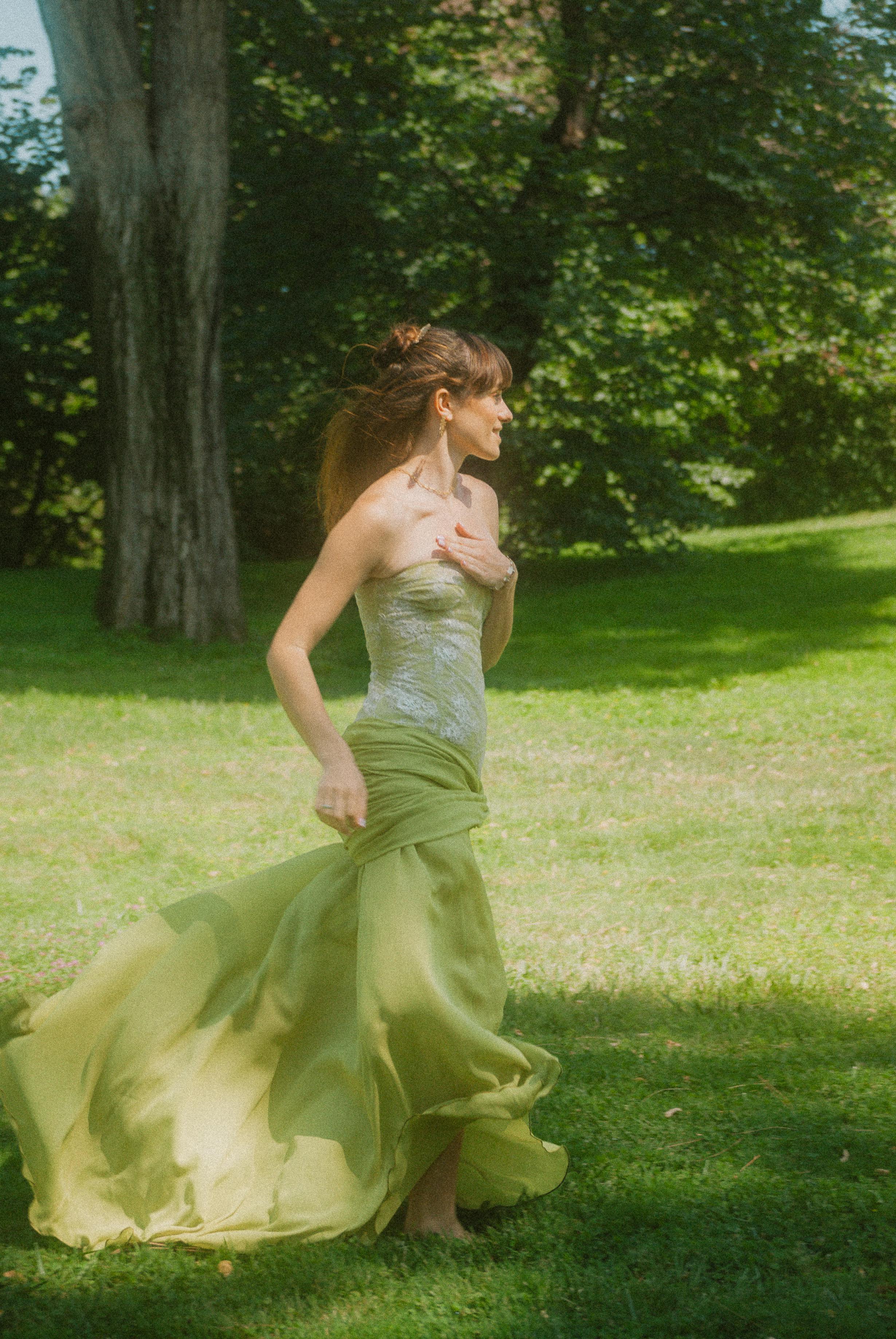 a woman in a green dress walking through a park