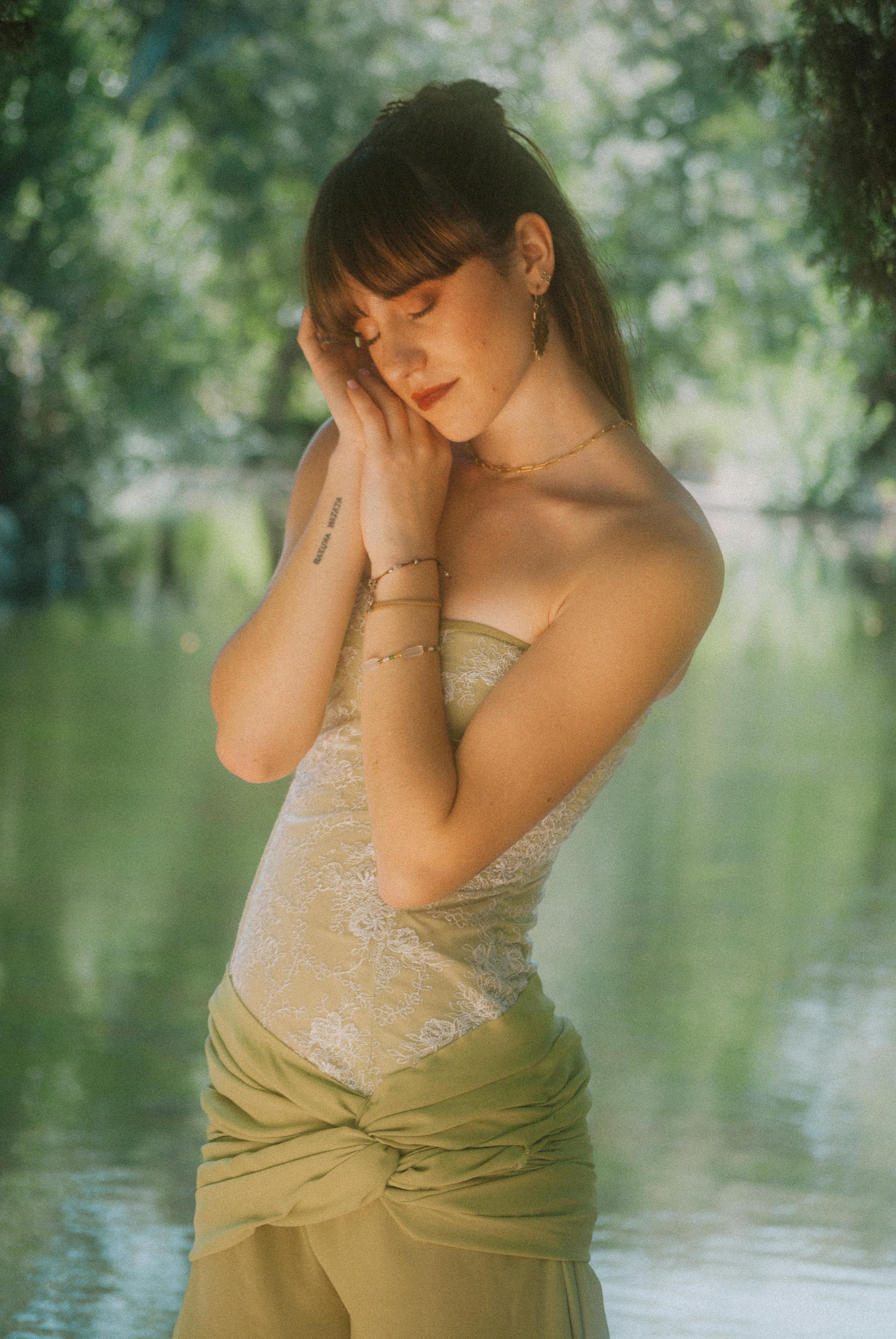 A serene portrait of a brunette woman in nature, eyes closed, posing by a river.