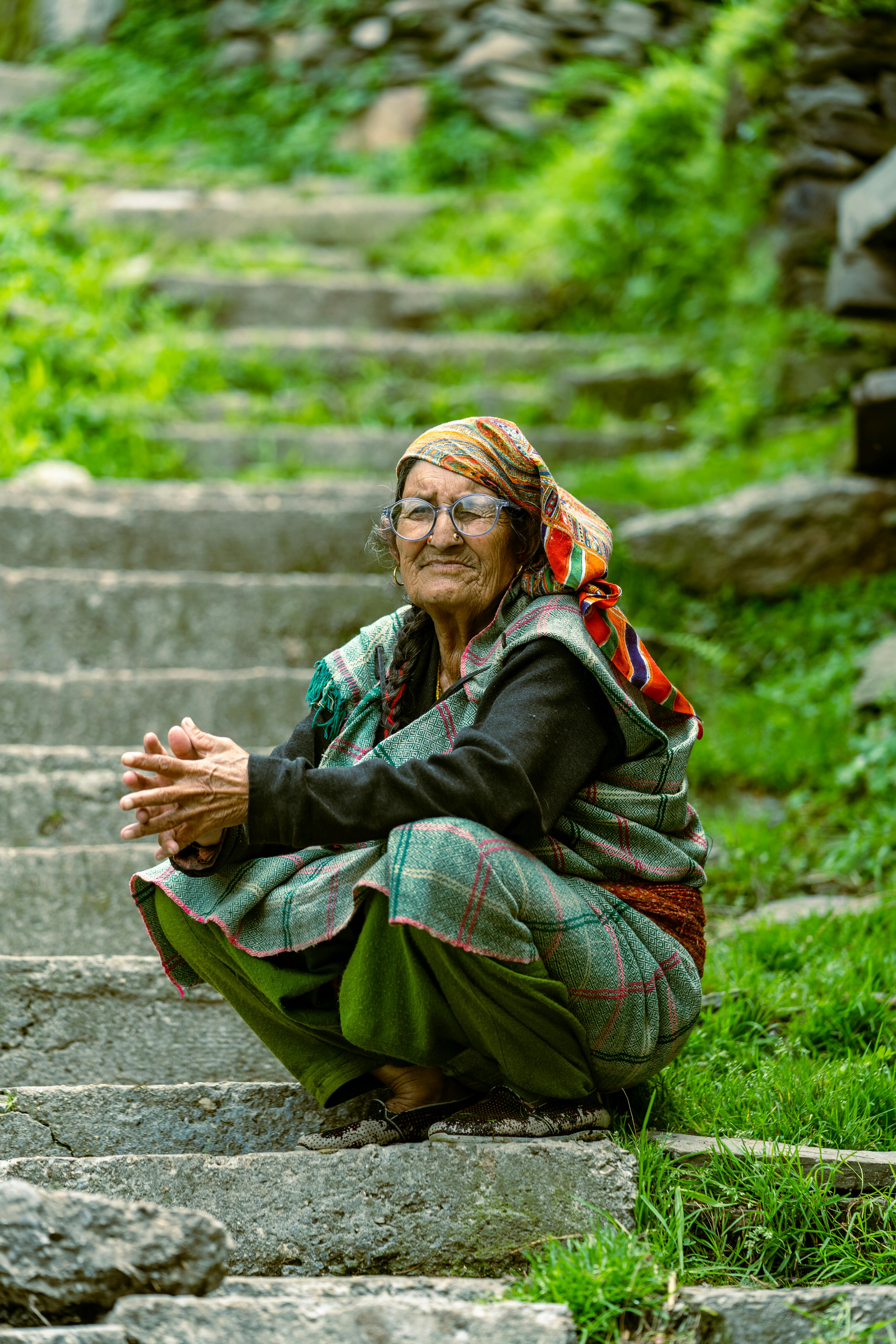 A woman in traditional attire sits peacefully on stone steps in a lush, green outdoor setting.